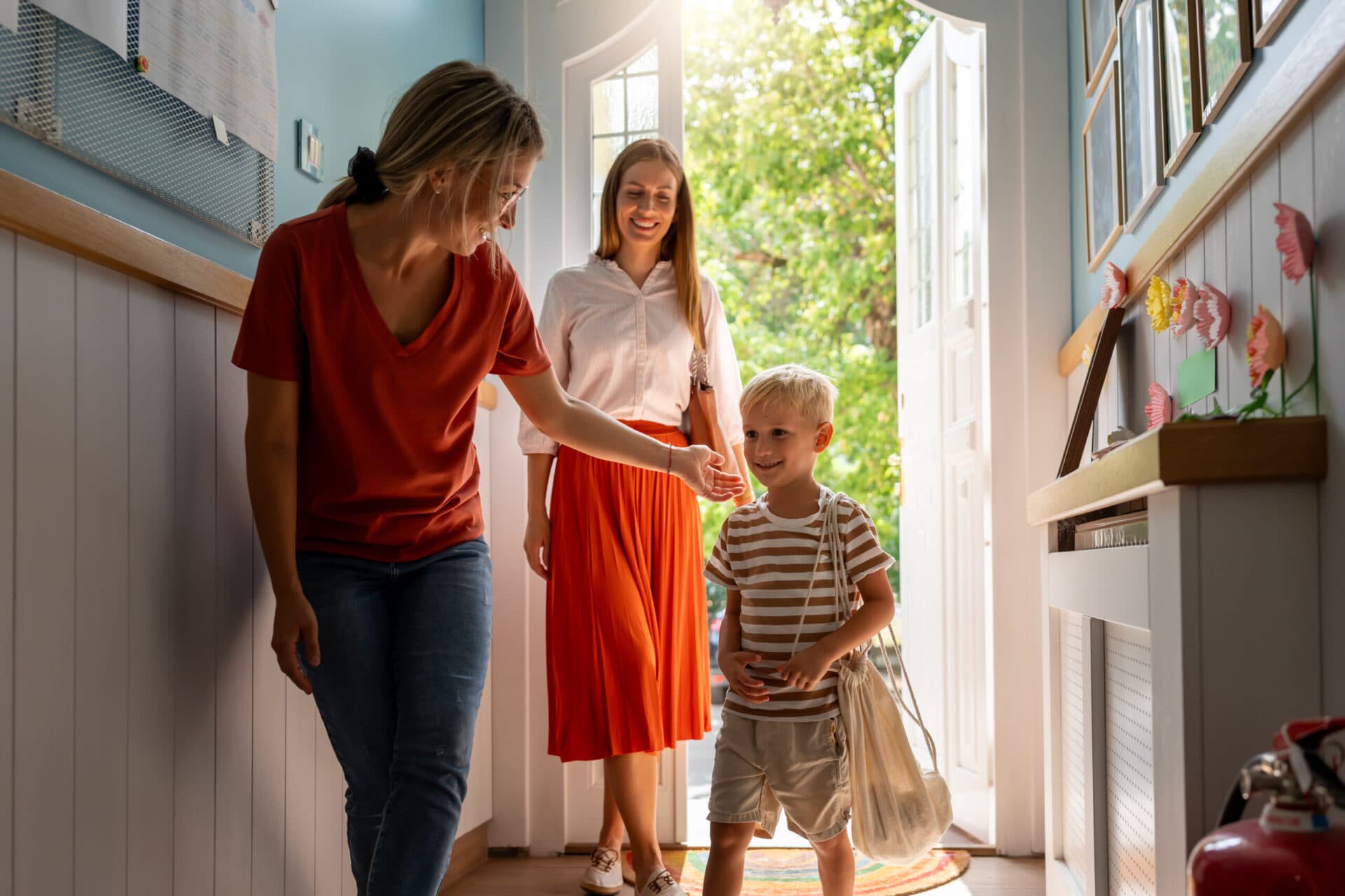 A teacher welcoming a child and their parent through the entryway at drop-off