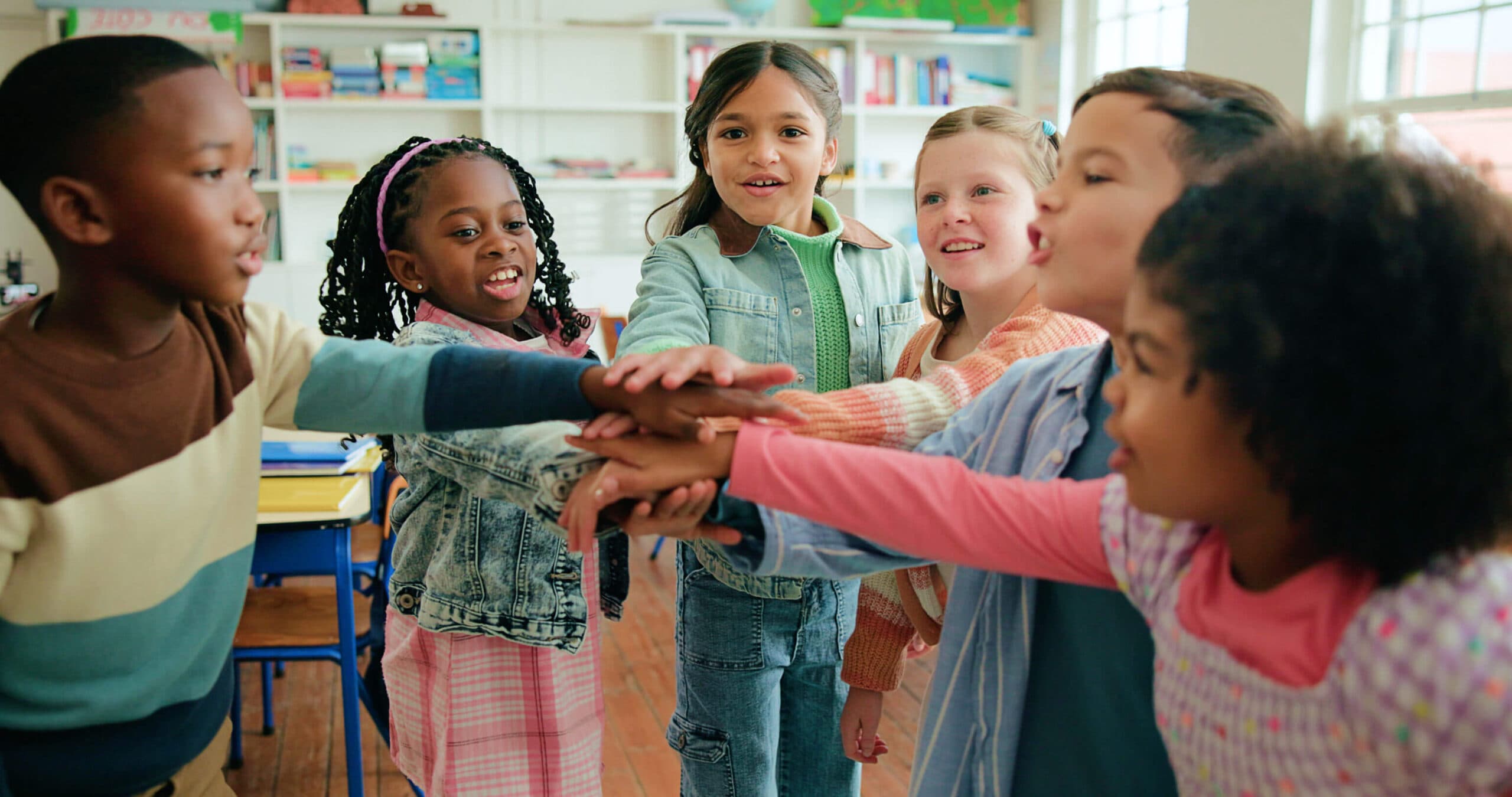 Six children smiling as they stack their hands together in the middle of a circle