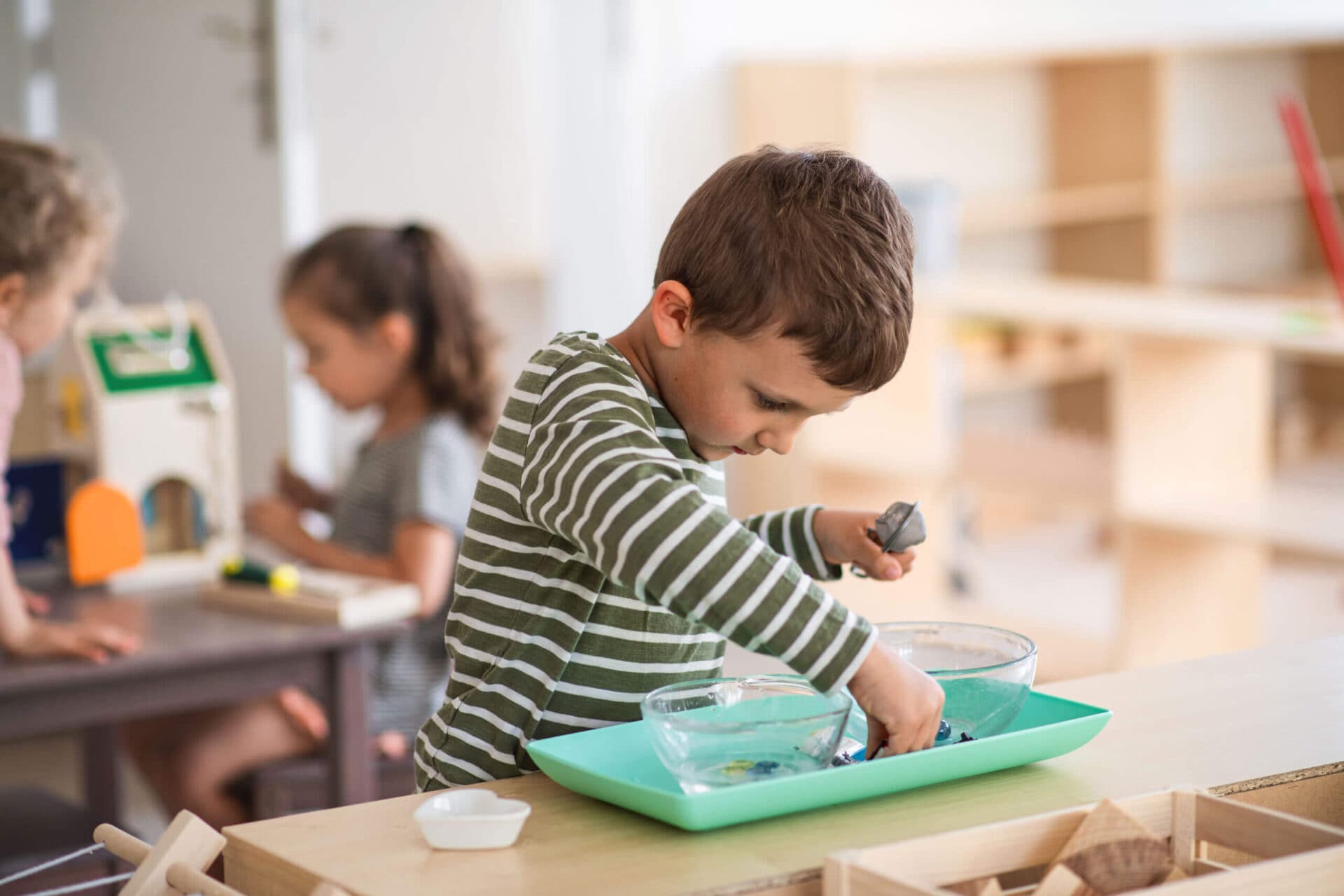 A boy leaning over a tray of water bowls, dropping small objects in to watch them sink