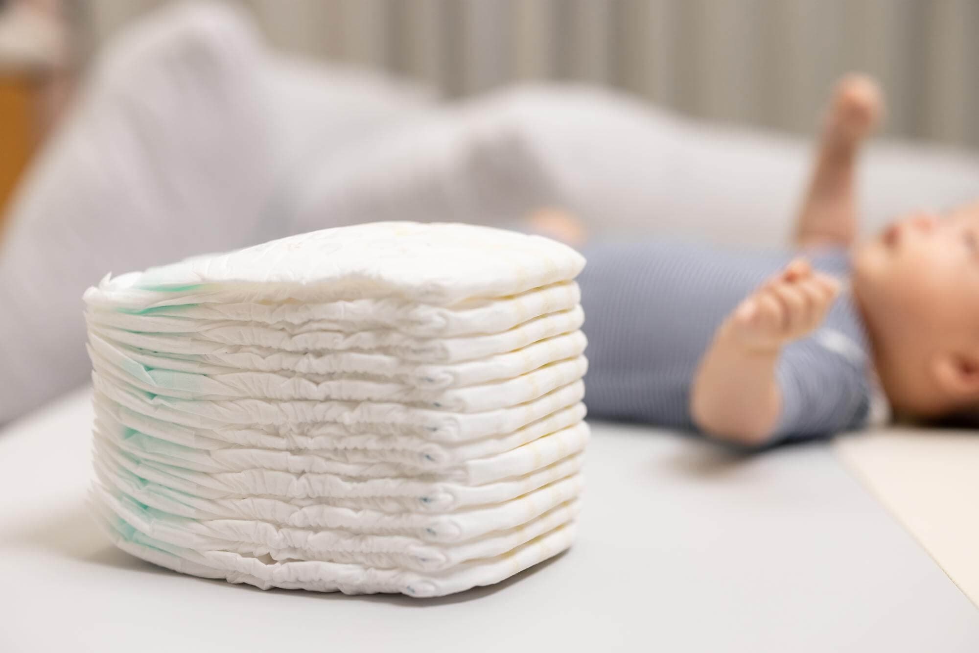 A neat stack of clean diapers on a changing table with a baby resting nearby