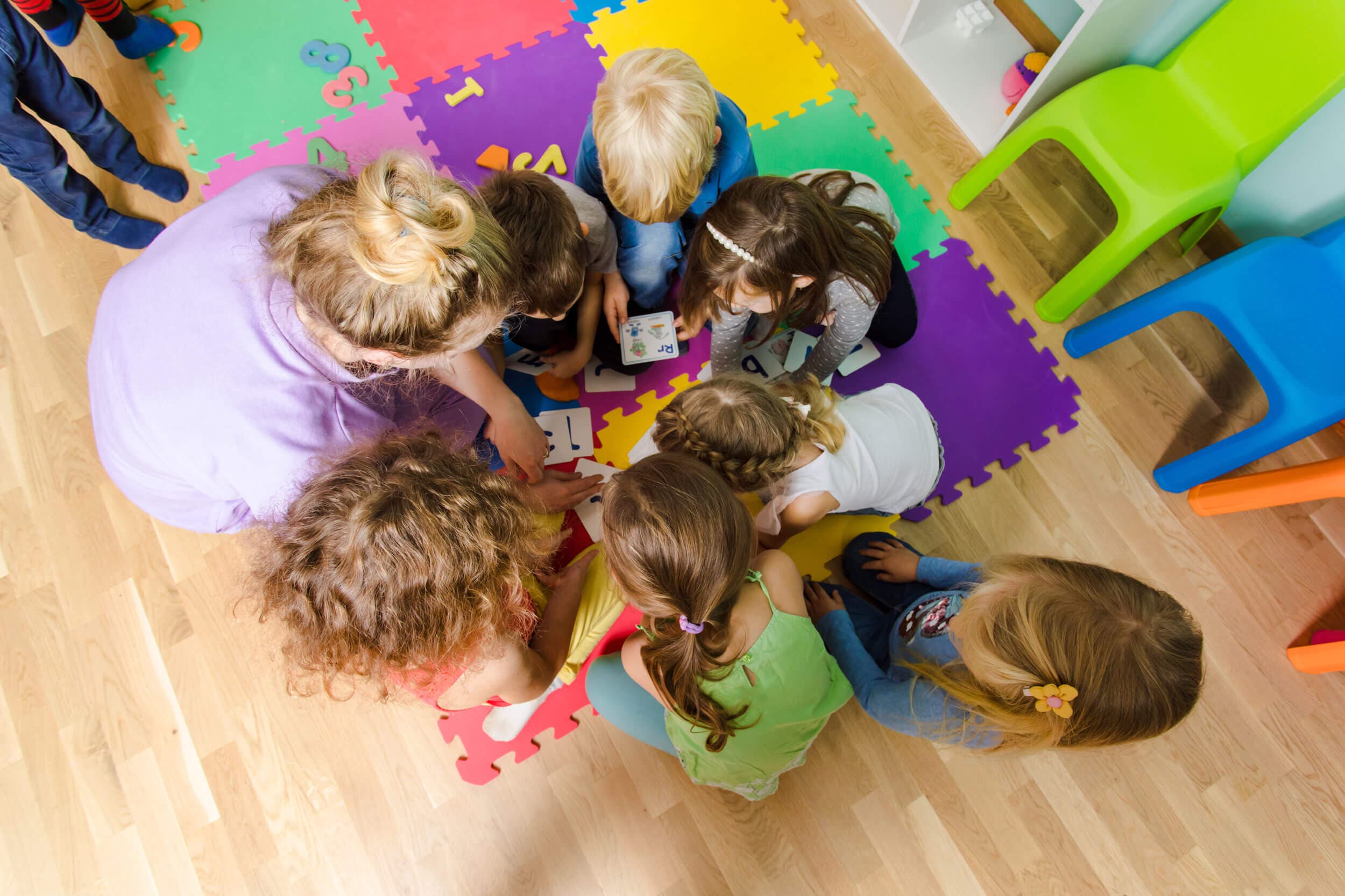 Overhead view of teachers and children gathered in a circle on a foam letter mat