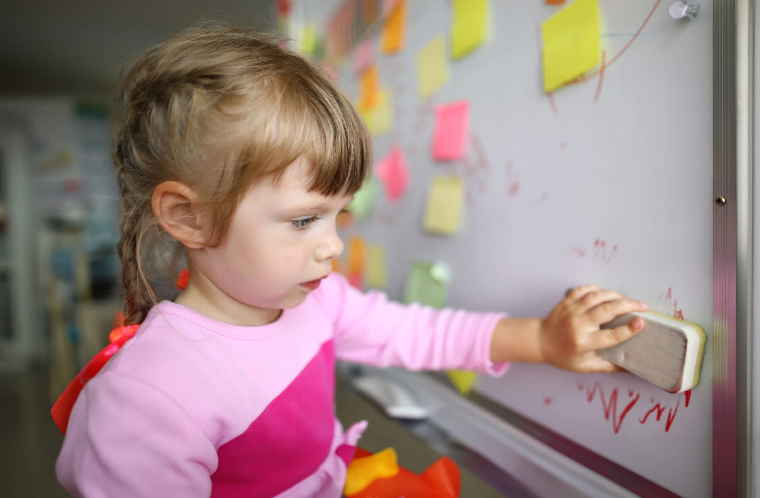 A girl reaching up to wipe a whiteboard clean with an eraser