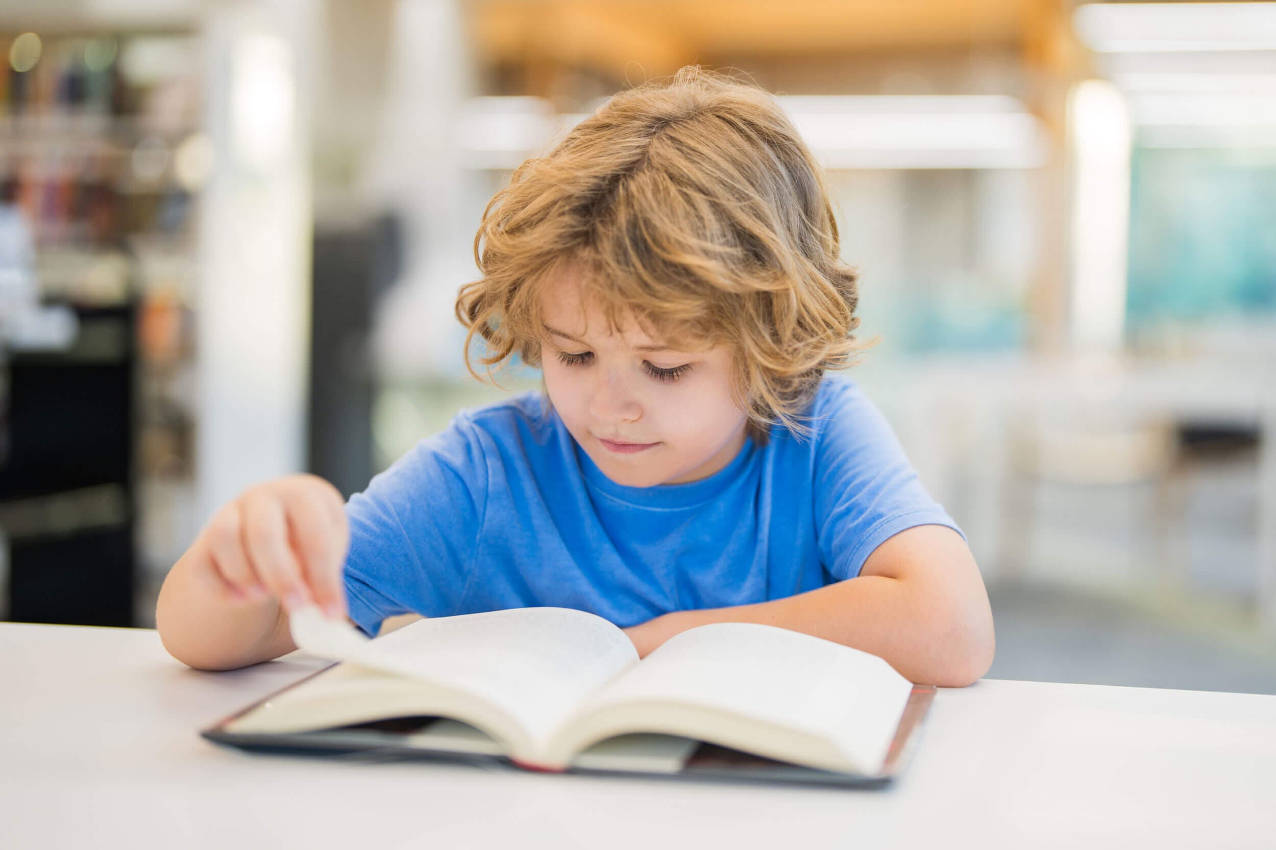A boy in a blue t-shirt turning the page of a large open book