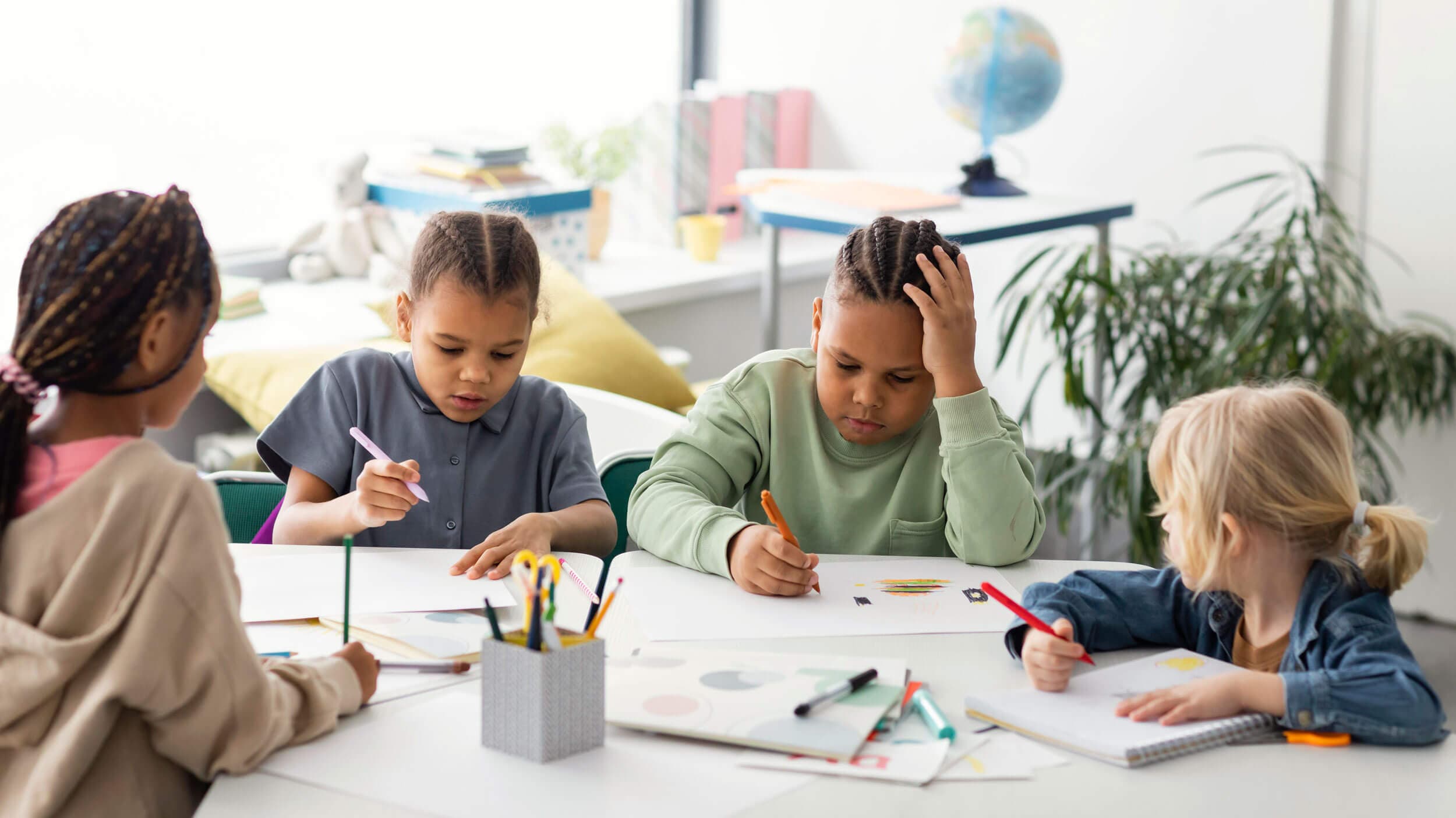 Four school-age children working on drawings and notebooks around a shared table