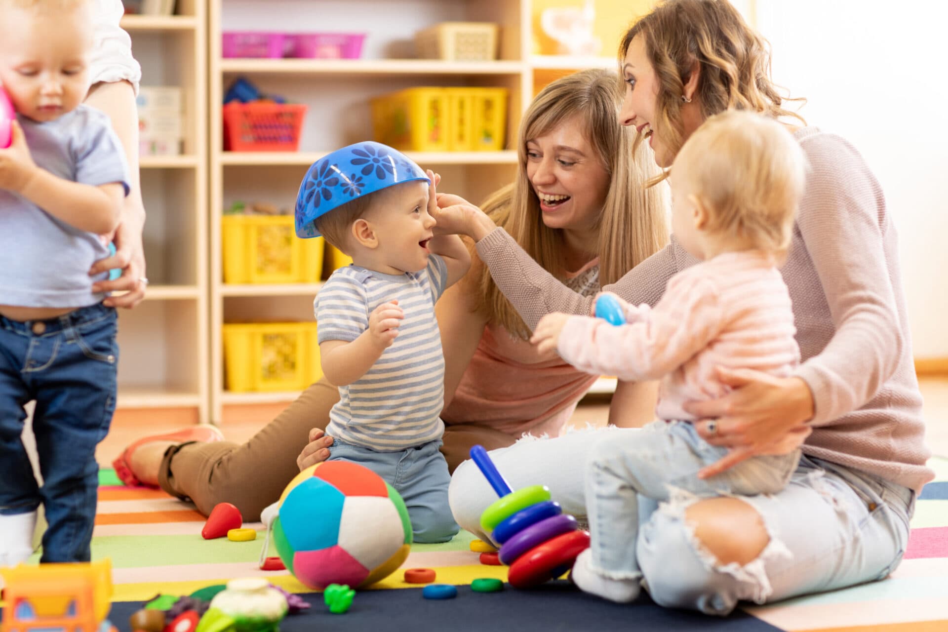 Two parents sitting on the playroom floor, laughing and playing with their children