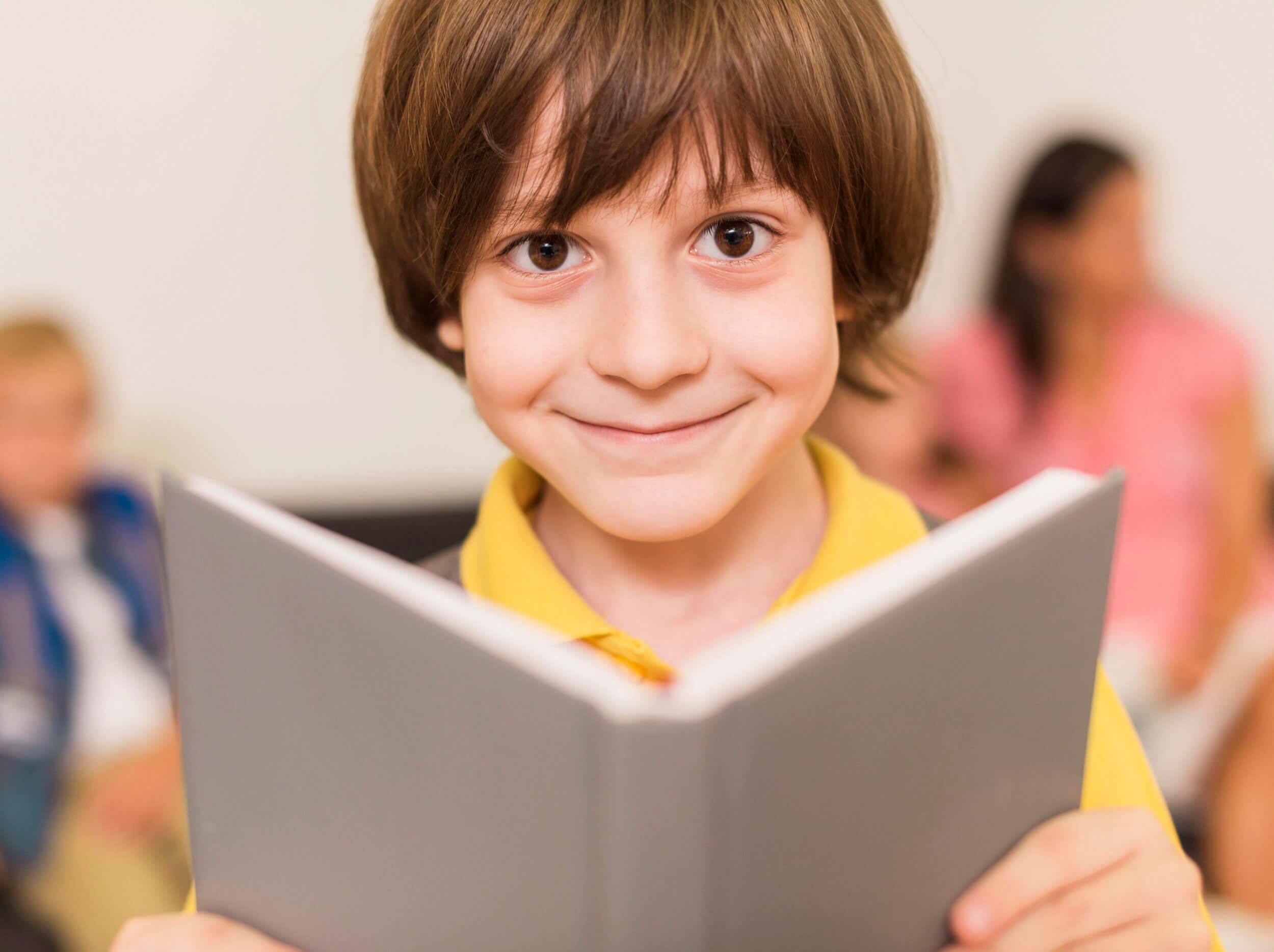 A smiling boy holding an open book up toward the camera