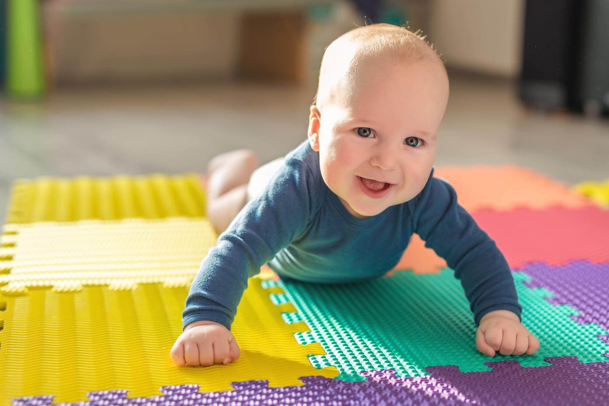 A smiling baby propped up on his arms during tummy time on a foam play mat