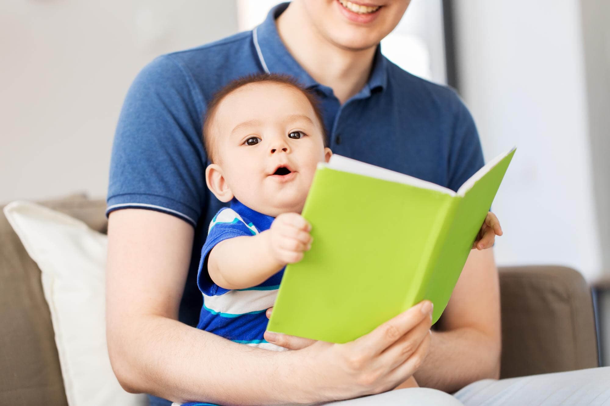 A father holding his baby on his lap while reading from a bright green book