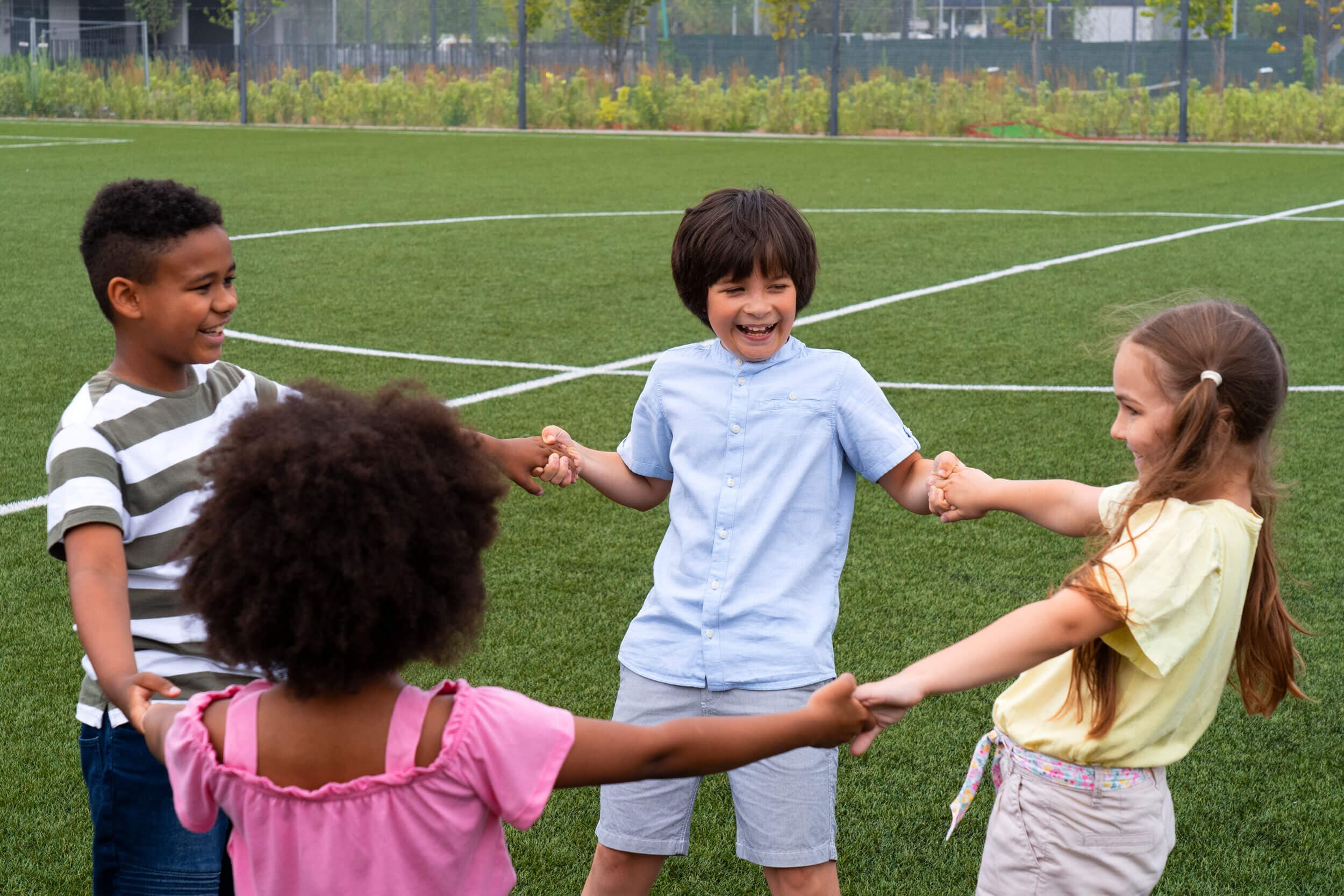 Four children holding hands in a circle and laughing on a grass field