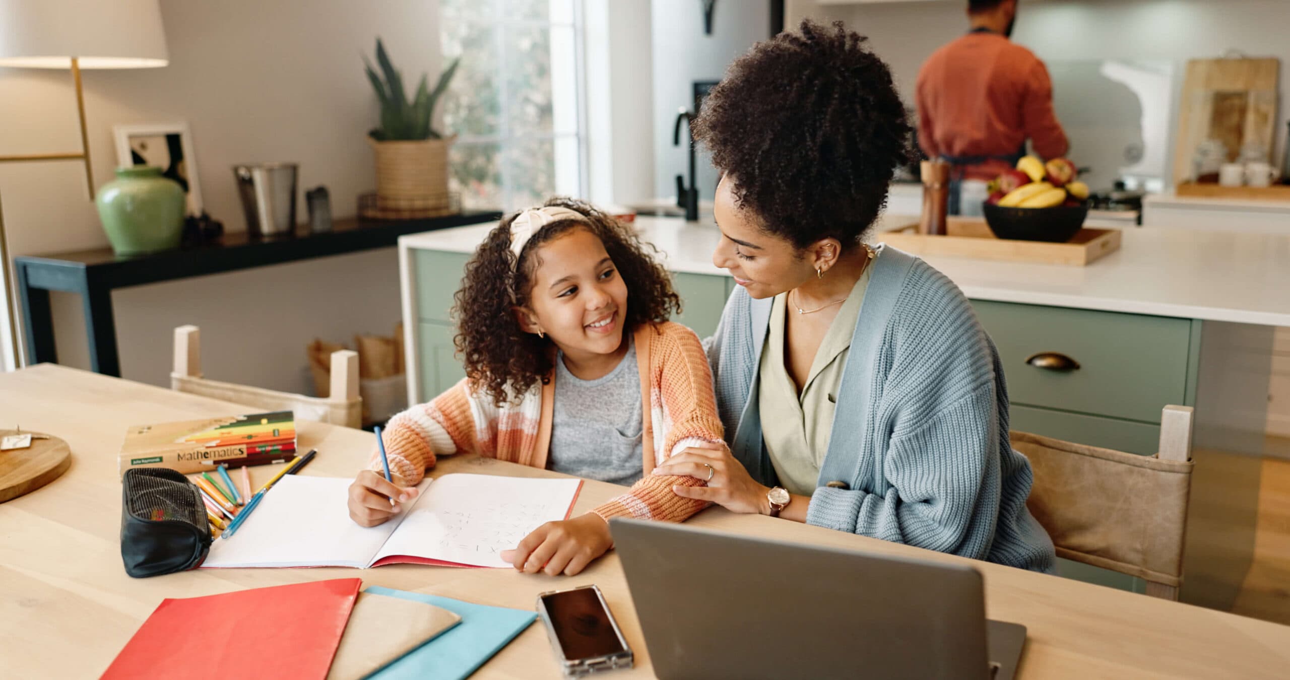 A mother and daughter smiling at each other over homework at the kitchen table